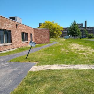 A sunny day showcasing a brick building adjacent to a grassy area with a path leading through it.