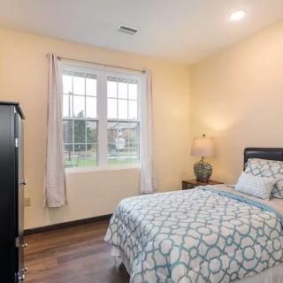 A cozy bedroom with a neatly made bed, soft lighting from a lamp, and natural light streaming through the window.
