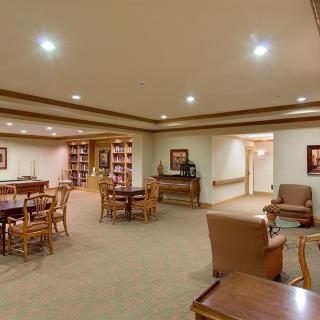A cozy library room with tables, chairs, and bookshelves.