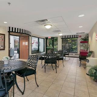 A cozy dining area with tables and chairs, featuring large windows and decorative plants.
