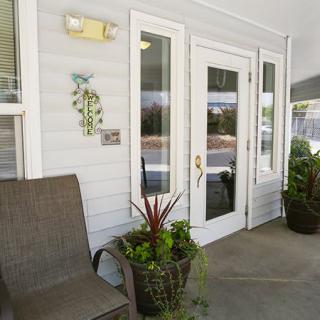 A welcoming porch area with a glass door, outdoor chair, and decorative plants.