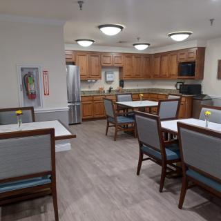 A spacious kitchen and dining area with wooden cabinets, modern lighting, and neatly arranged tables and chairs.