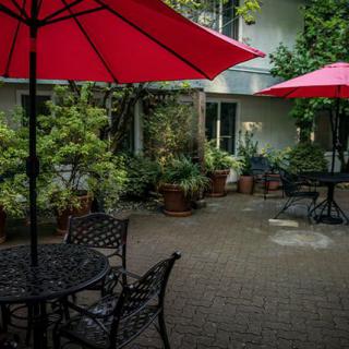 A cozy patio area featuring red umbrellas and wrought iron furniture surrounded by lush greenery.