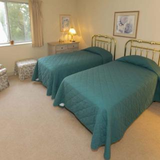 A cozy bedroom with twin beds featuring green bedspreads and a nightstand with a lamp.
