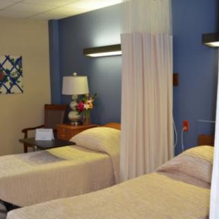 A hospital room with twin beds separated by a curtain and decorated with a floral arrangement on the side table.