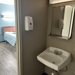 A view of a small bathroom area with a sink and mirror, leading into an adjacent hotel room.