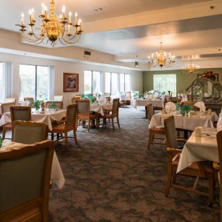 A spacious dining room with elegantly set tables and ornate chandeliers.