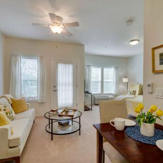 A bright and cozy living room featuring a comfortable sofa, coffee table, and dining area, illuminated by natural light.