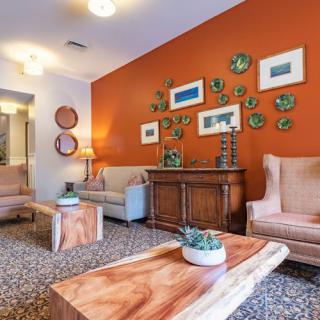 A stylish living room featuring an orange accent wall adorned with artwork, and comfortable seating arrangements.