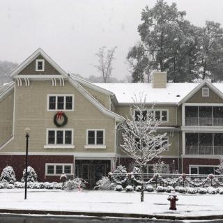 A snow-covered house with a festive wreath, surrounded by trees in a winter landscape.