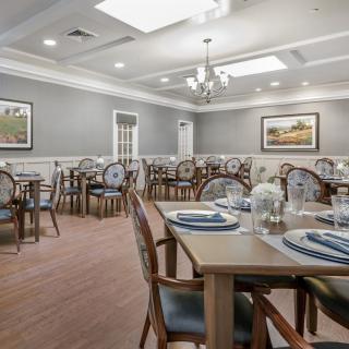 A well-lit dining room with neatly arranged tables and chairs, featuring elegant place settings and decorative artwork on the walls.