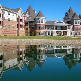A modern residential building with a castle-like design reflected in a calm lake.