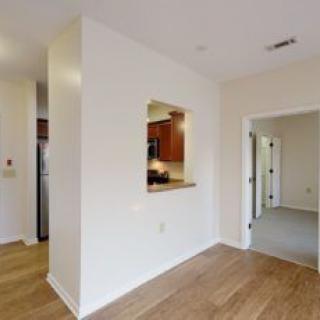 A modern interior featuring an open layout with a view into the kitchen, showcasing hardwood floors and neutral colors.