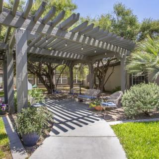 A serene outdoor patio area with a pergola, surrounded by lush greenery and comfortable seating.