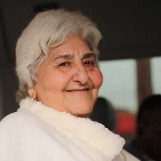 A smiling elderly woman with gray hair and a white scarf.