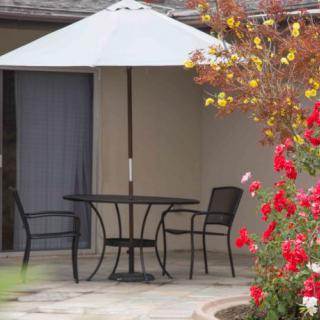 A cozy patio setup featuring a table and chairs beneath an umbrella, surrounded by colorful flowers.
