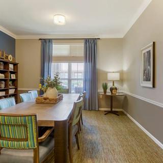 A well-decorated dining room with a wooden table and chairs, complemented by blue curtains and a bookshelf.