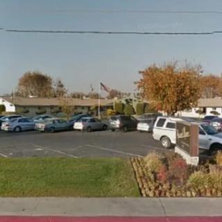 A parking lot filled with cars next to a building, surrounded by trees on a clear day.