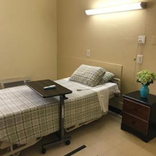 A simple hospital room featuring a bed, bedside table, and a small flower arrangement.