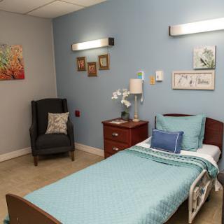 A cozy hospital room featuring a single bed, comfortable chair, and decorative wall art.