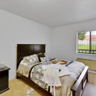 A cozy bedroom featuring a neatly made bed, nightstand, and a large window offering natural light.