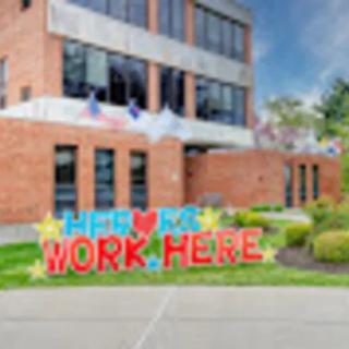 A colorful sign in front of an office building that reads 'We Love to Work Here'.