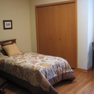 A simple bedroom with a single bed, wooden closet, and hardwood flooring.