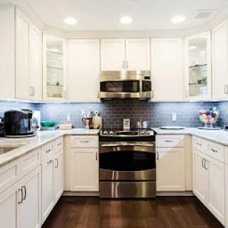 A modern kitchen featuring white cabinets, stainless steel appliances, and elegant wood flooring.