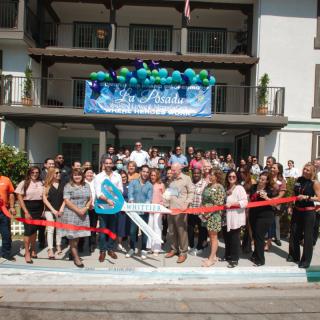 A group of people gathered for a ribbon-cutting ceremony in front of a building, decorated with balloons.