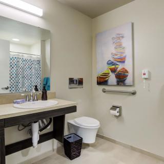 A modern bathroom featuring a sink, mirror, and wall art near the toilet and shower area.
