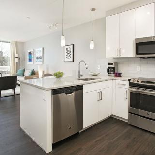 A modern kitchen with white cabinets and stainless steel appliances, featuring an island and open space design.
