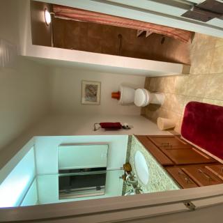 A bathroom with a sink and mirror in the foreground, and a toilet in the background.