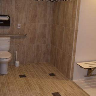 An accessible bathroom featuring a toilet, grab bars, and a shower bench.