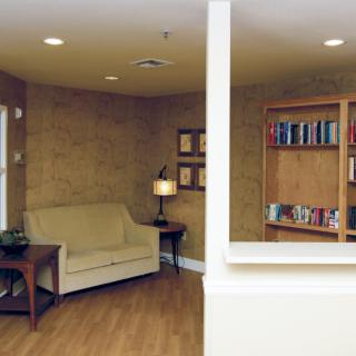 A cozy living room with a beige sofa, a bookshelf filled with books, and a lamp providing ambient lighting.