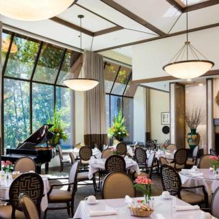 An elegant dining room with a grand piano, featuring large windows and sophisticated table settings.