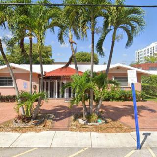 A suburban building with palm trees in front, featuring a parking area and a sidewalk.
