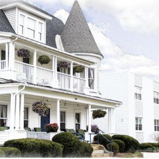 A charming Victorian-style house with a turret and spacious porch, adorned with hanging plants and lush landscaping.