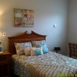 A cozy bedroom with a patterned bedspread, decorative pillows, and wall art.