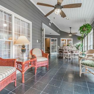 A cozy sunroom with wicker furniture, tiled floor, and ceiling fans.
