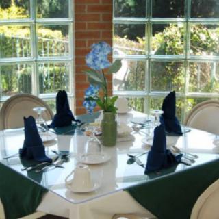 A neatly set dining table with blue napkins and a floral centerpiece in a bright, windowed restaurant area.