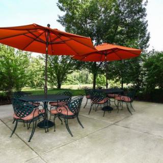 A well-furnished patio with tables and chairs under vibrant orange umbrellas, surrounded by lush greenery.