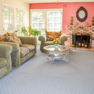 A cozy living room with a green sofa set, coffee table, and a brick fireplace, illuminated by natural light from large windows.