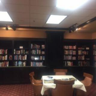 A cozy library reading room with bookshelves and a table surrounded by chairs.