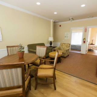 A cozy living room with a dining area, featuring a round wooden table surrounded by chairs, a comfortable sofa, and a lamp.
