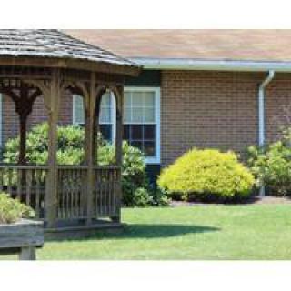 A wooden gazebo in a well-maintained garden with a brick building in the background.