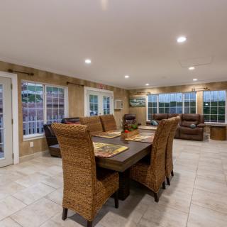 A spacious dining room with wicker chairs and a rectangular table, surrounded by large windows.