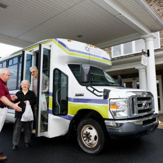 An elderly person being assisted while exiting a bus at a building entrance.