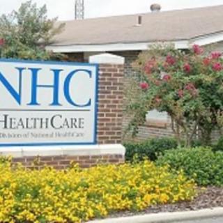 An NHC HealthCare sign in front of a building with landscaped flowers.