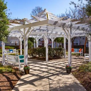 A sunlit pergola with outdoor seating in a garden setting.