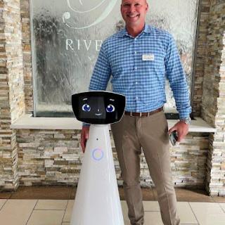 A man standing next to a friendly-looking robot in a modern lobby.